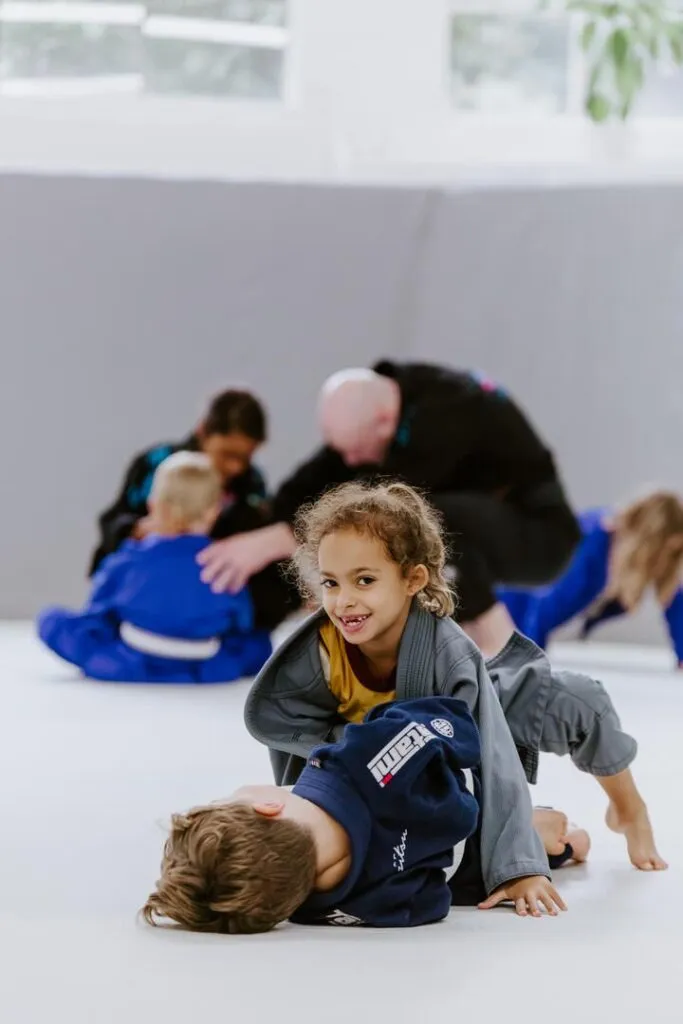 A young girl smiles while practicing a controlled position with a training partner during a kids BJJ class at SuperFly BJJ in Decatur