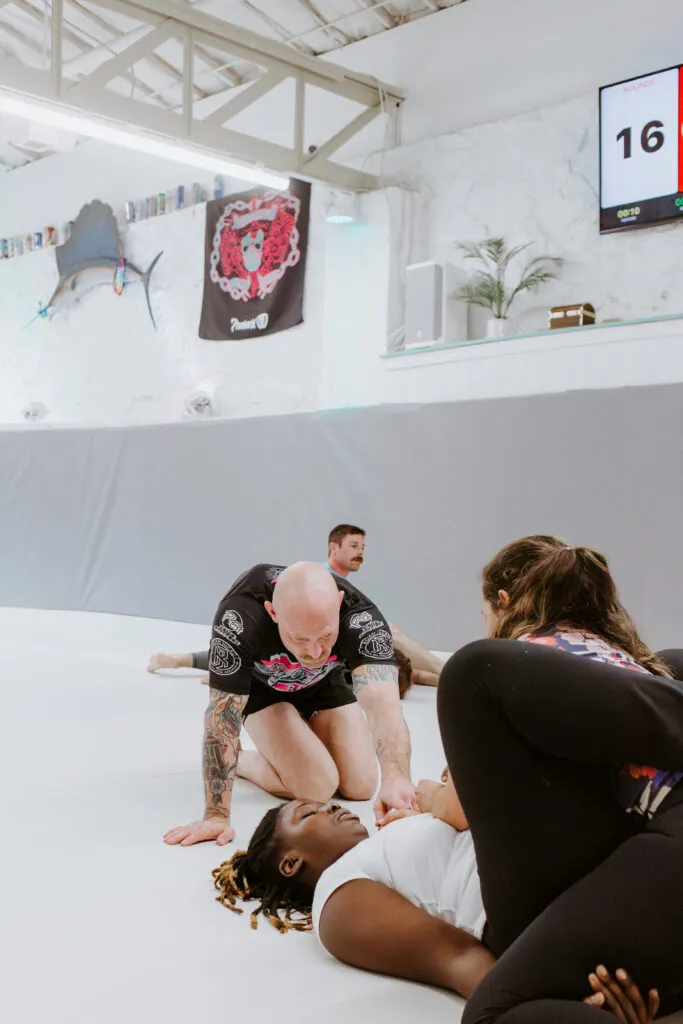 An instructor working closely with two women on a BJJ technique during the Intro to BJJ/101 class at SuperFly BJJ Decatur