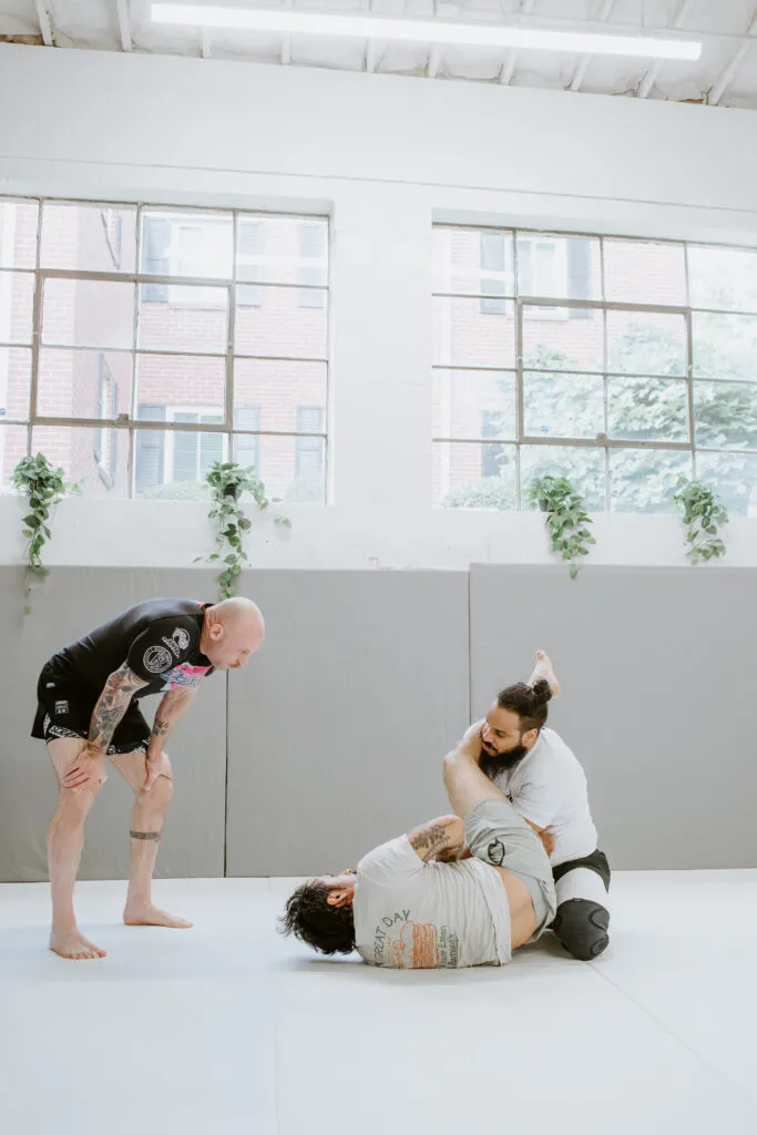 Instructor helping two students during an adult beginner martial arts class at SuperFly BJJ in Decatur.