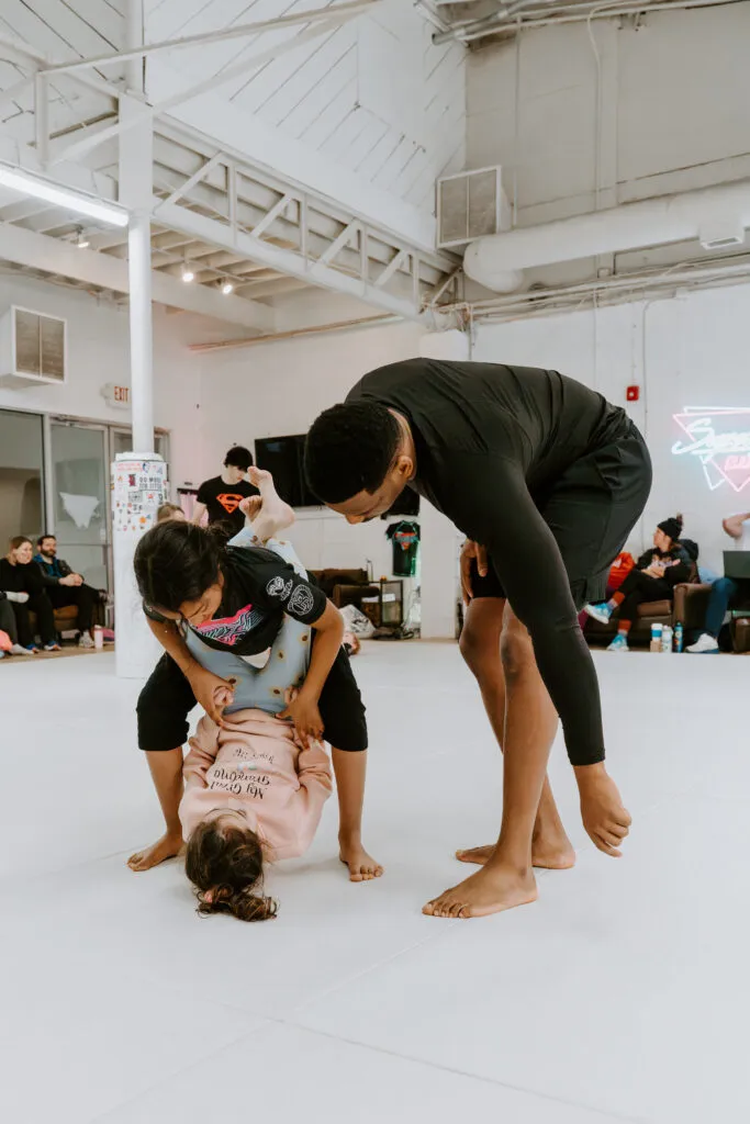 An instructor helps two kids learn a technique during a kids BJJ class at SuperFly BJJ in Decatur, GA.