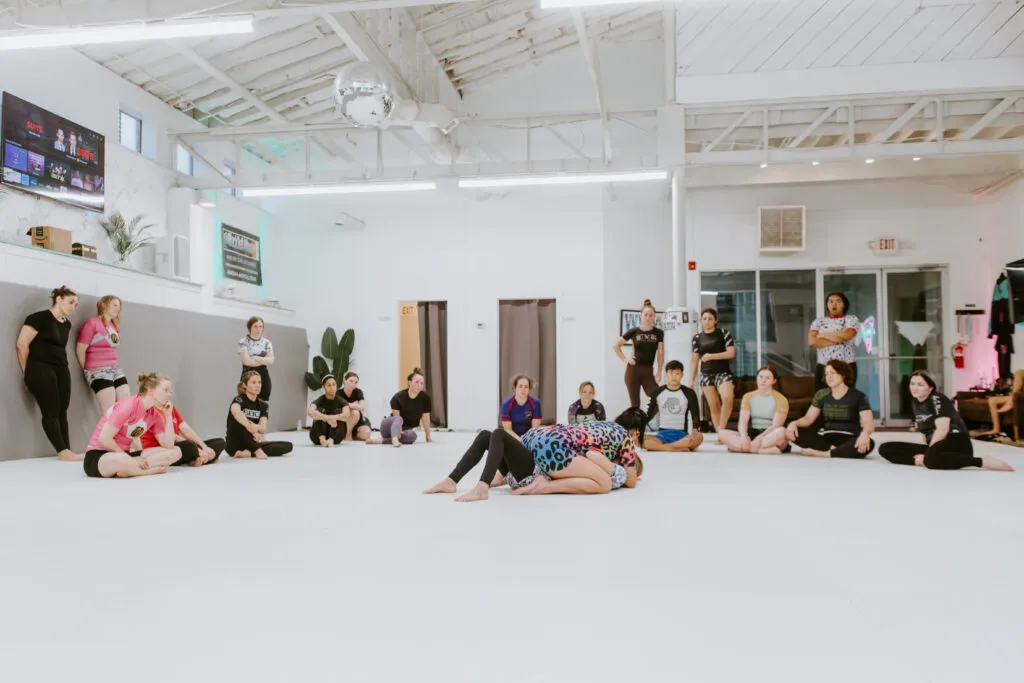 A female instructor is demonstrating the technique of the evening to a group of students during a women-only BJJ class at SuperFly BJJ in Decatur, GA.