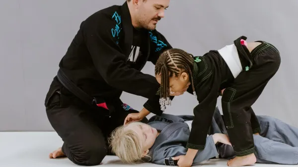 An instructor helping two young kids in kimonos learn a technique