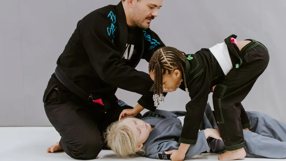 A BJJ instructor helping two young kids in kimonos learn a technique at SuperFly BJJ