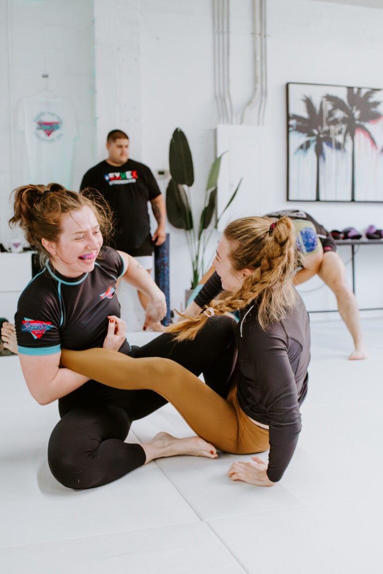 Two girls practicing Brazilian Jiu-Jitsu together and laughing.