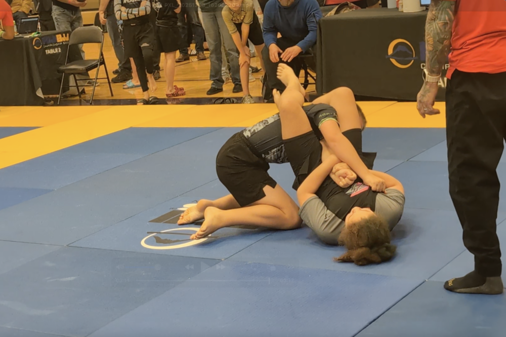SuperFly BJJ kids competition team member submitting an opponent with an armbar in a tournament.