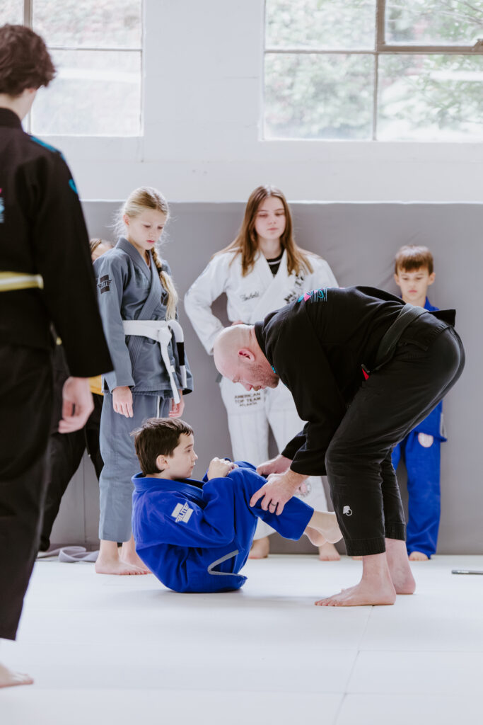 Older kids learning Brazilian Jiu-Jitsu techniques with instructor guidance during the Kids 7+ BJJ class.
