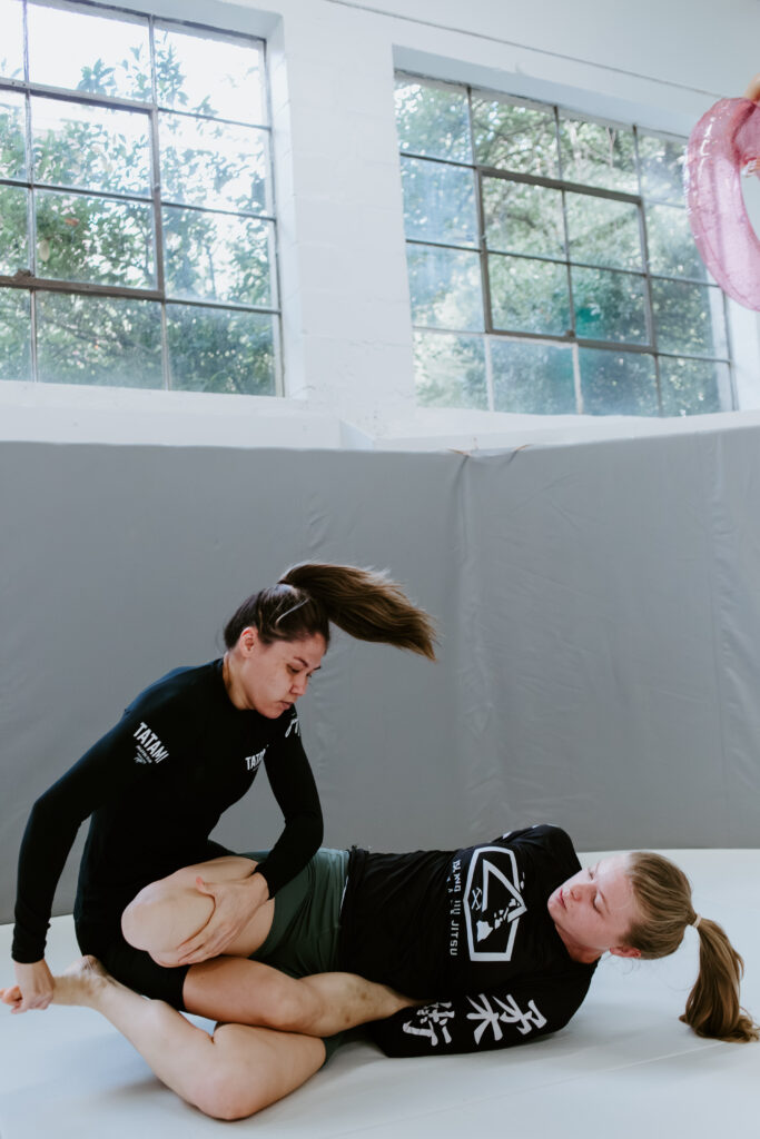 Two women practicing Brazilian Jiu-Jitsu ground techniques during the women-only BJJ class at SuperFly BJJ Decatur.