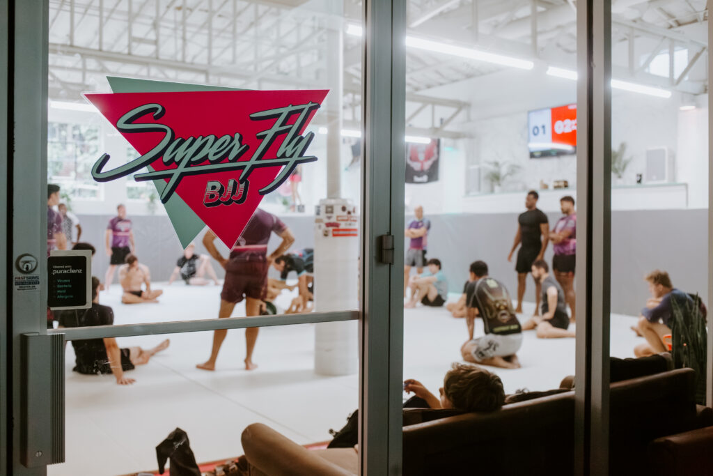 Picture of the entrance to SuperFly BJJ in Decatur. It shows a martial arts class through the front doors of the school.