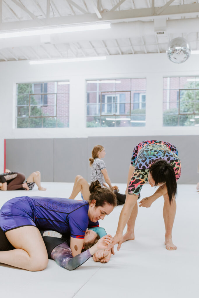 A female instructor assisting two female students during a women-only martial arts class at SuperFly BJJ in Decatur.